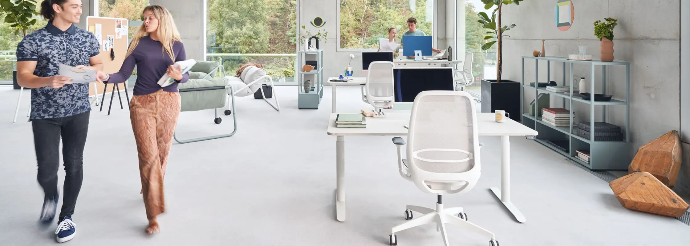 Zwei Personen gehen durch ein helles Büro mit Sitzecke und Drehstühlen