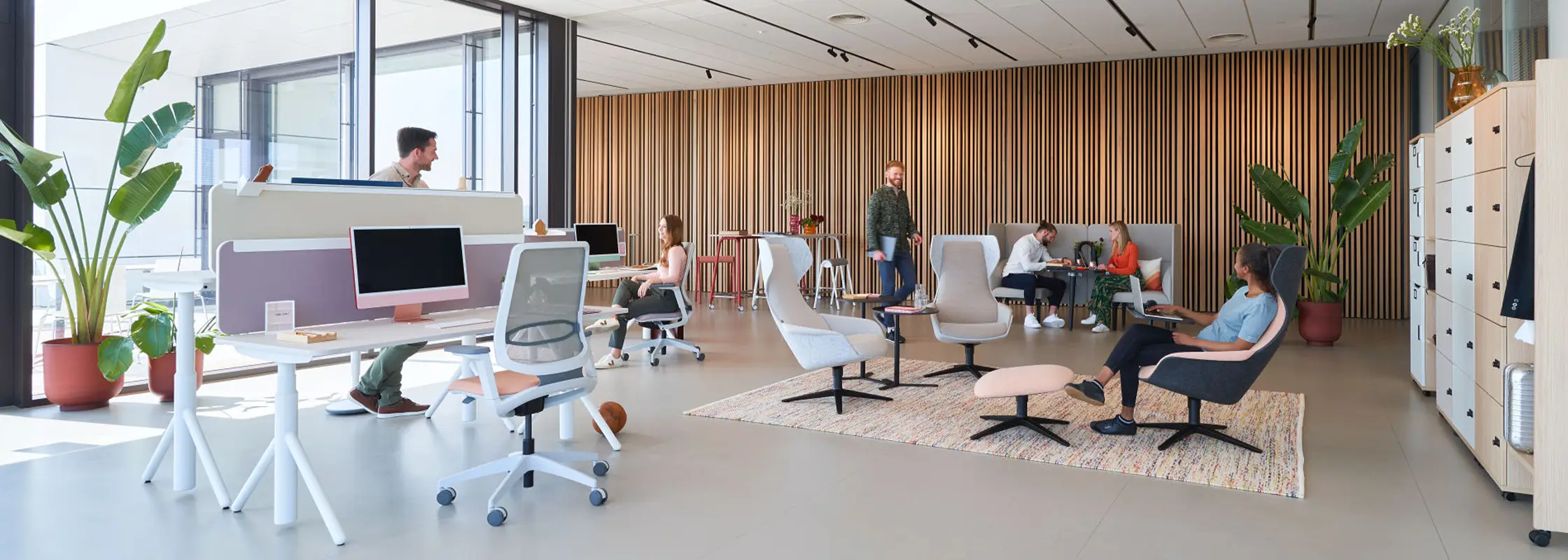 Bürofläche mit Holzlamellenwand, Loungesesseln und höhenverstellbaren Tischen