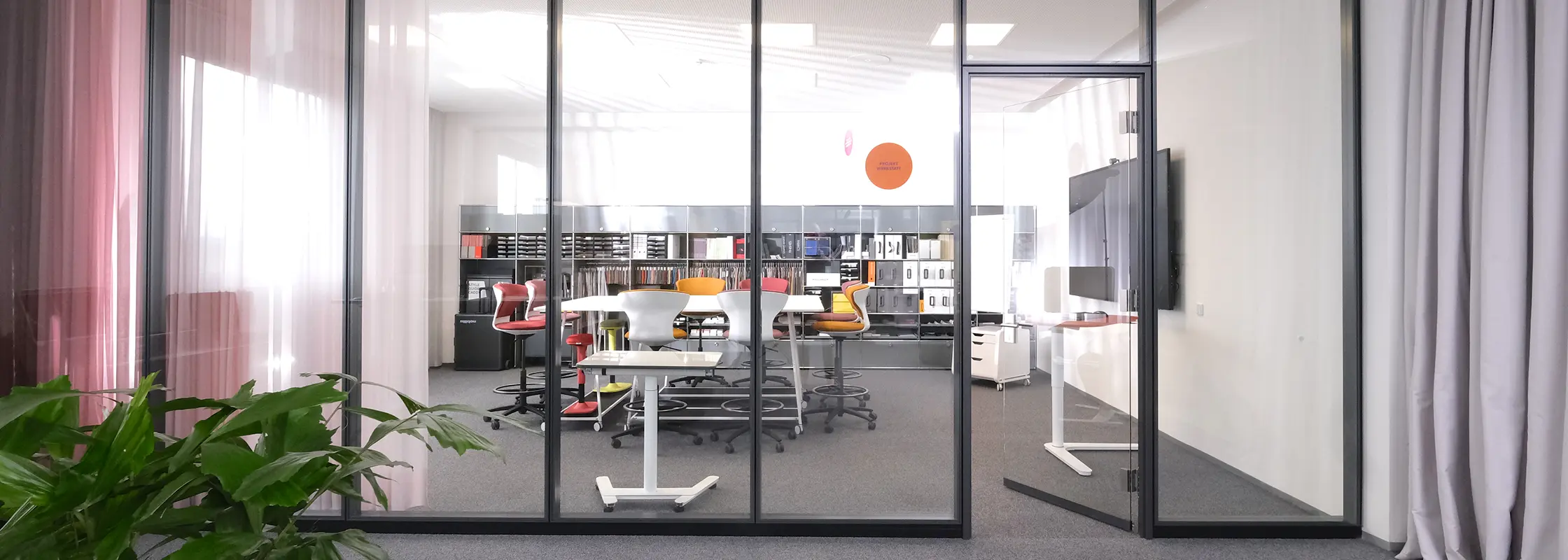 Blick durch die Glaswand in den Showroom mit Musterregalen und Arbeitsplätzen