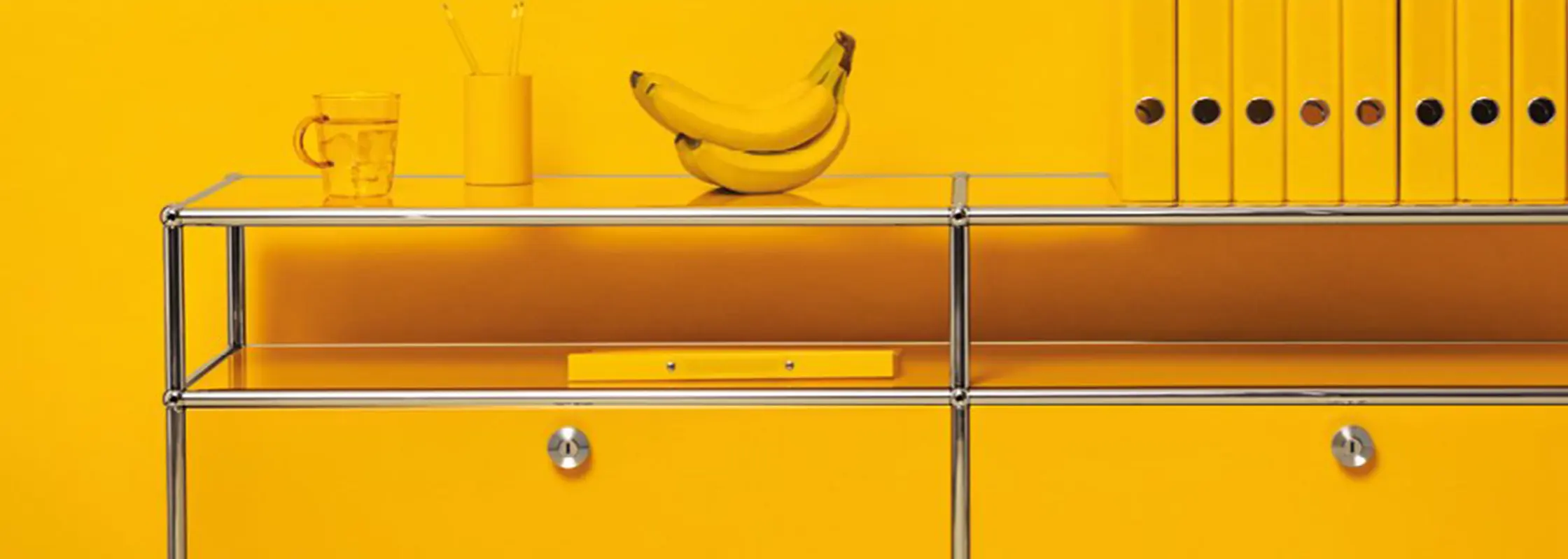 Gelbes USM-Haller-Sideboard vor gelber Wand mit Ordnern und Bananen