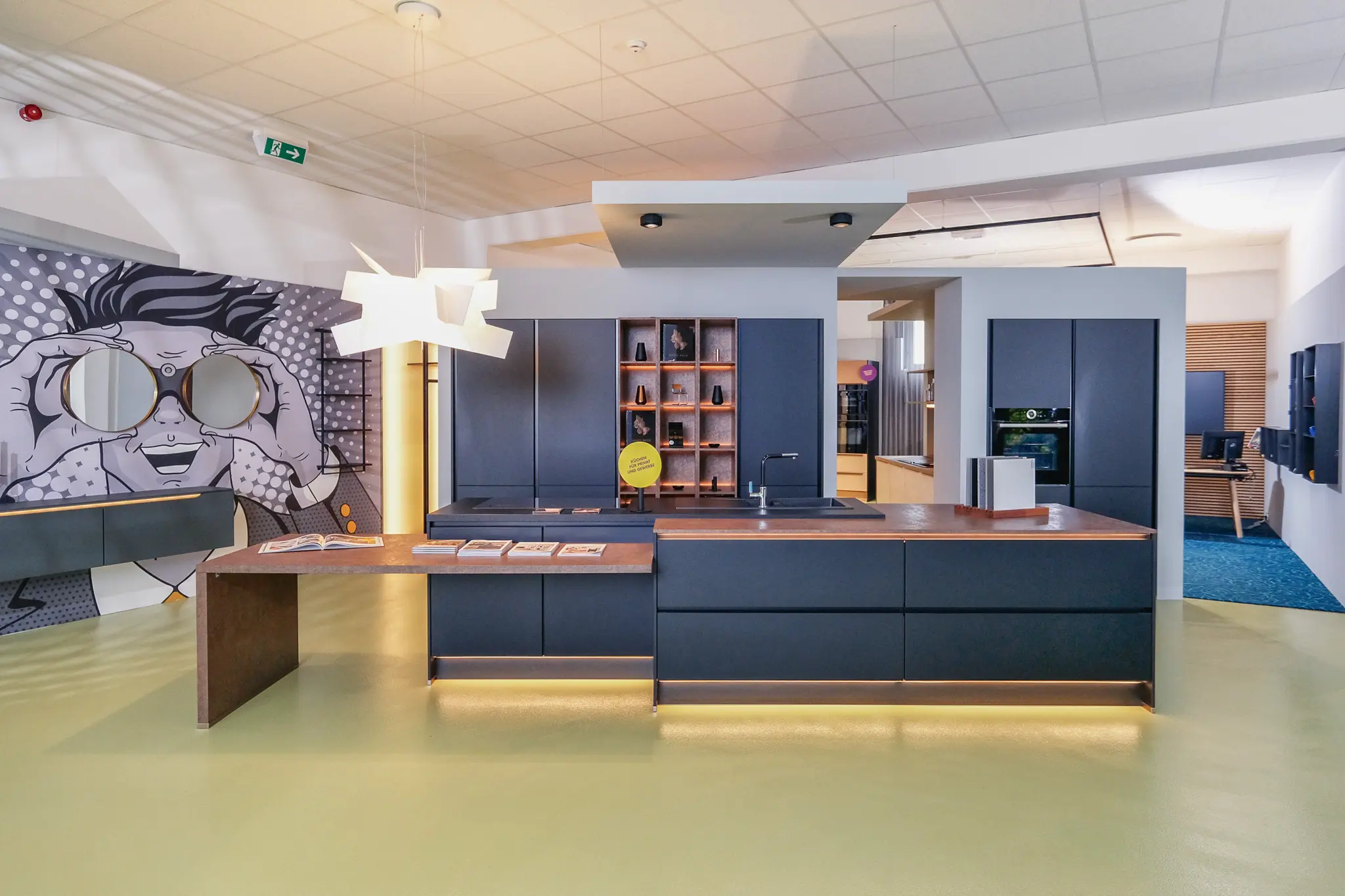 Küchenausstellung im Showroom mit dunkelblauer Kochinsel und Wandbild