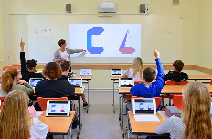 Klassenzimmer mit Tablets auf den Tischen, Lehrerin an der Projektionsfläche