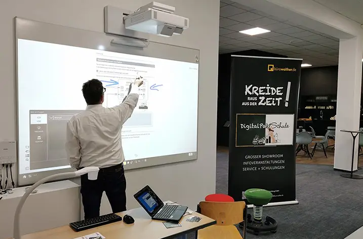 Mann bedient ein interaktives Whiteboard neben dem Rollup „Kreide raus aus der Zeit“