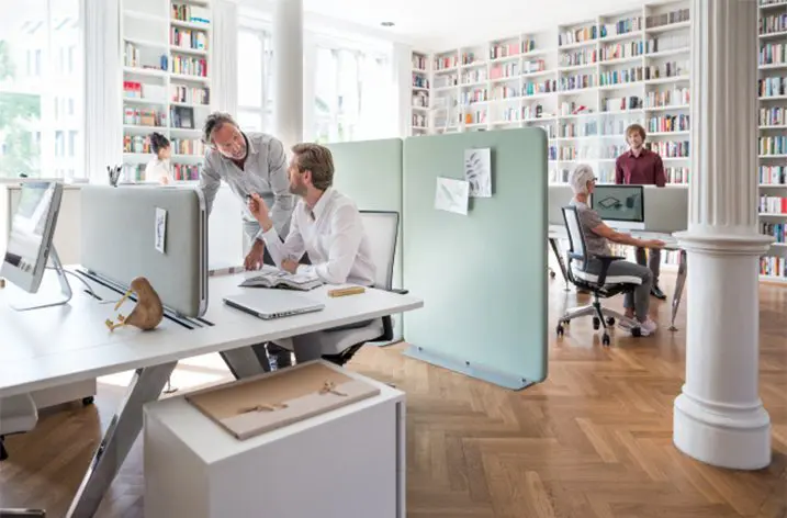 Zwei Männer im Gespräch an Arbeitsplätzen mit Trennwänden in einer Bibliothek