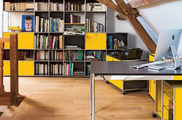 Dachgeschossbüro mit gelb-schwarzem USM-Haller-Regal voller Bücher und Schreibtisch