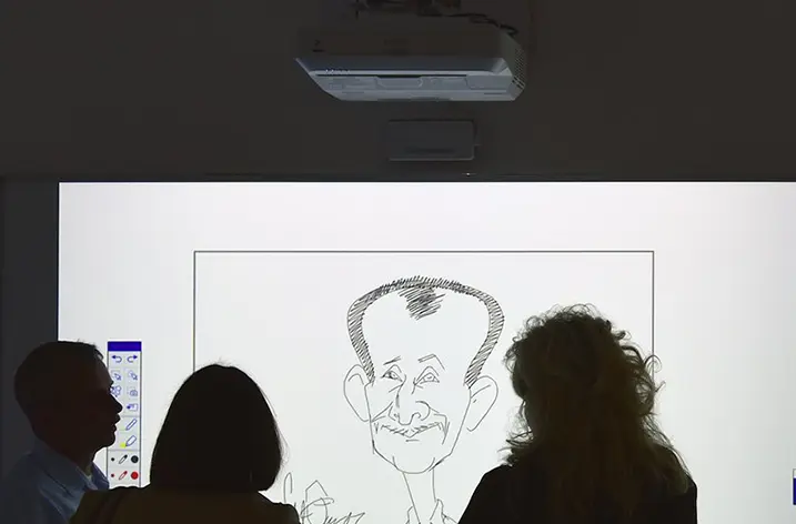 Besucher vor einer Projektion, auf der eine Porträtkarikatur entsteht
