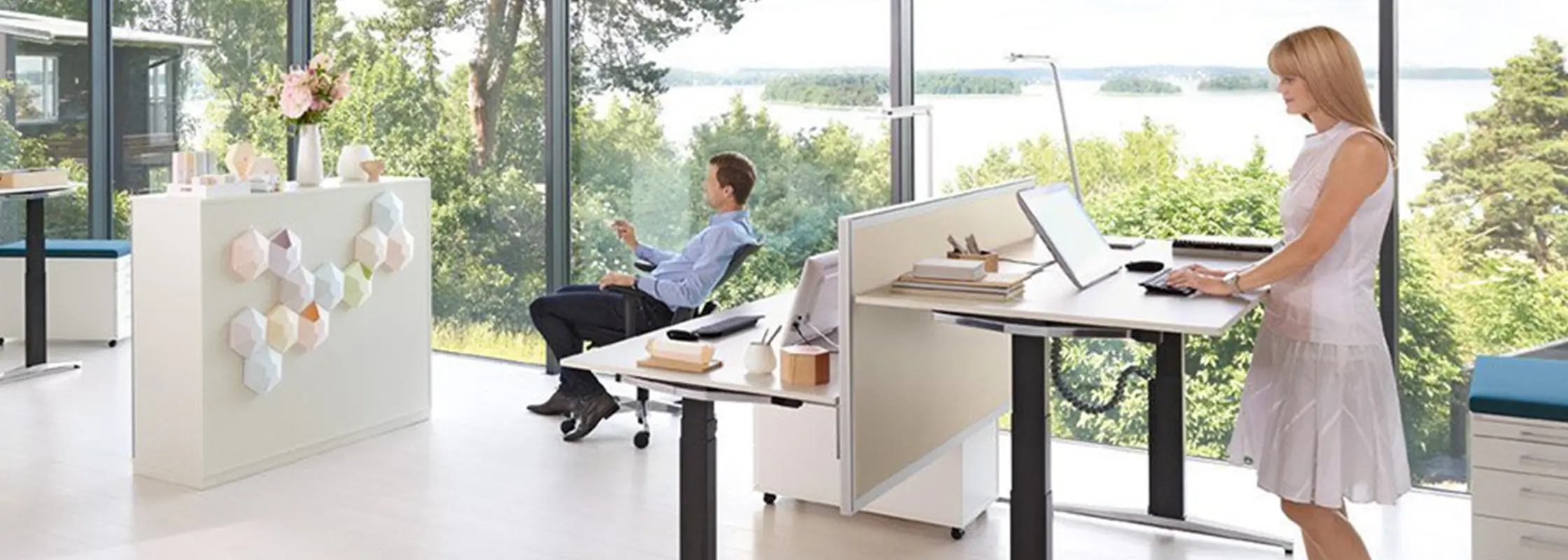 Mann sitzt am Schreibtisch vor einem Panoramafenster mit Blick auf Wasser und Bäume