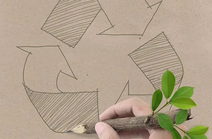 Hand zeichnet mit einem Ast das Recycling-Zeichen auf Packpapier